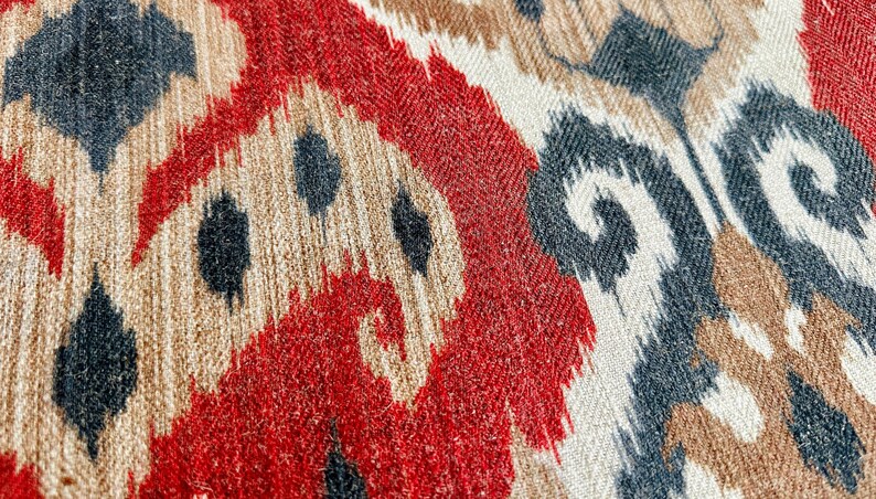 May include: Close-up of a fabric with a red, white and black ikat pattern. The fabric has a textured, woven appearance.