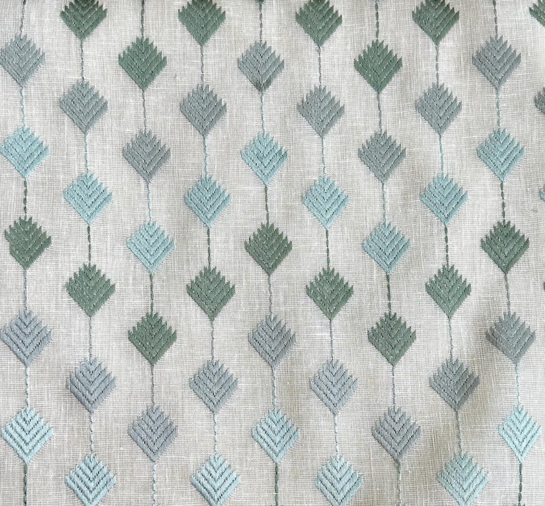 May include: A white fabric with a repeating pattern of blue and green diamond shapes. The diamonds are made of a series of small, embroidered lines.