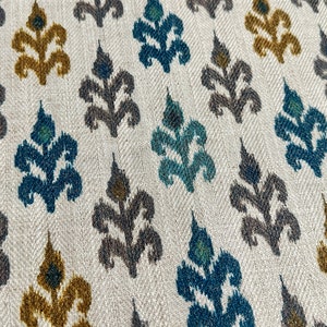 May include: A white fabric with a repeating pattern of stylized floral motifs in shades of teal, brown, and gold.