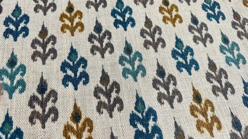 May include: A white fabric with a repeating pattern of stylized floral motifs in shades of teal, brown, and gold.