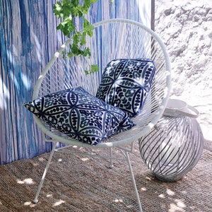 May include: White outdoor chair with a round back and two blue and white patterned pillows. The chair is sitting on a woven rug in front of a blue and white striped wall.