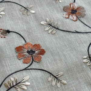 K&ouml;nnte beinhalten: Nahaufnahme eines durchsichtigen Stoffes mit gestickten Blumenmustern in Braun-, Orange- und Wei&szlig;t&ouml;nen. Der Stoff hat eine subtile Textur und ein zartes, feminines Gef&uuml;hl.