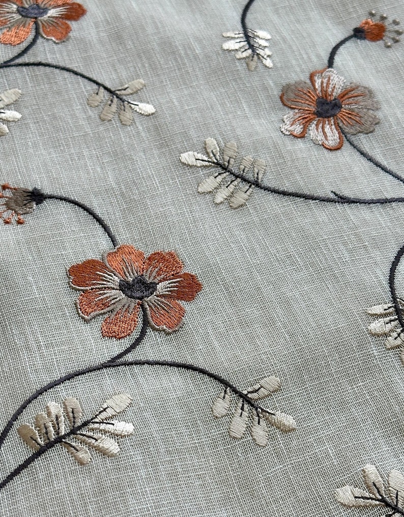 K&ouml;nnte beinhalten: Nahaufnahme eines durchsichtigen Stoffes mit gestickten Blumenmustern in Braun-, Orange- und Wei&szlig;t&ouml;nen. Der Stoff hat eine subtile Textur und ein zartes, feminines Gef&uuml;hl.