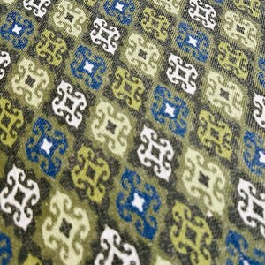 May include: A close-up of a fabric with a repeating pattern of green, blue, and white geometric shapes. The fabric has a textured surface.
