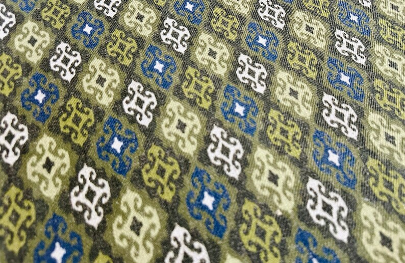 May include: A close-up of a fabric with a repeating pattern of green, blue, and white geometric shapes. The fabric has a textured surface.