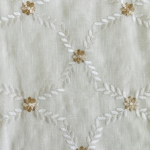 May include: White fabric with a delicate embroidered pattern of small flowers and leaves in a light brown color.