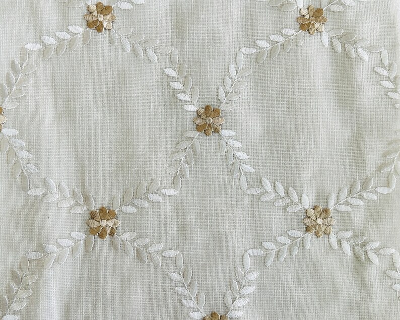 May include: White fabric with a delicate embroidered pattern of small flowers and leaves in a light brown color.