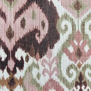 May include: Close-up of a fabric with an ikat pattern. The design features repeating abstract shapes in shades of brown, pink, and green on a white background. The fabric has a textured appearance, suitable for upholstery or home decor.