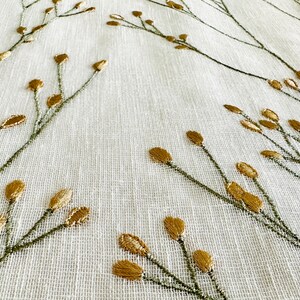 May include: White fabric with a subtle texture featuring an embroidered pattern of green stems and gold leaves.