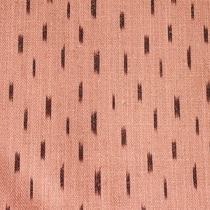 Puede incluir: Primer plano de una tela rosa con un patr&oacute;n ikat negro. La tela tiene un tejido de espiga sutil.