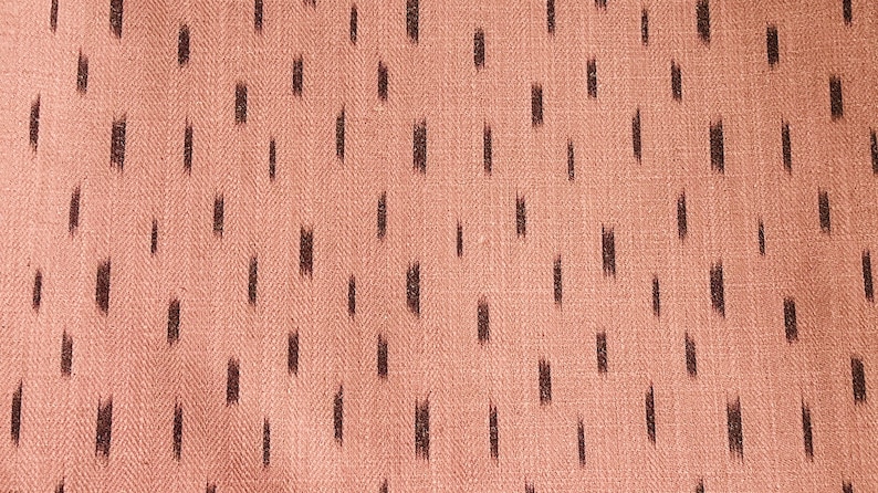 Puede incluir: Primer plano de una tela rosa con un patr&oacute;n ikat negro. La tela tiene un tejido de espiga sutil.