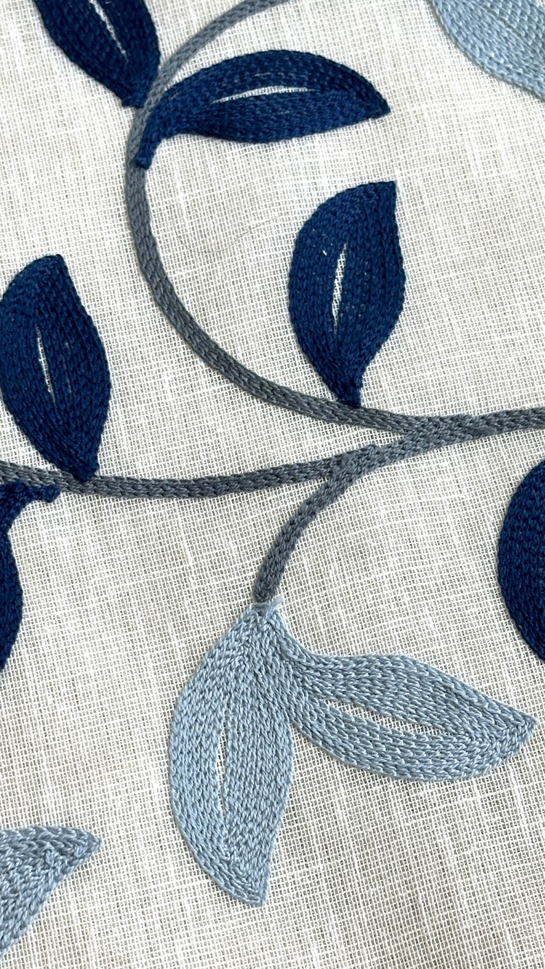 May include: A close-up of a white fabric with blue and gray embroidered leaves. The leaves are stitched in a detailed pattern, creating a delicate and elegant design.