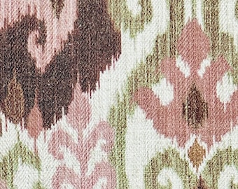 May include: Close-up of a woven fabric with an ikat design. The pattern features repeating shapes in shades of brown, pink, green, and white. The fabric has a textured appearance, suggesting a natural fibre.