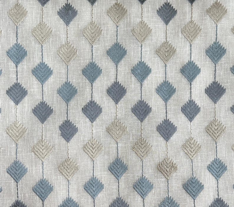 Puede incluir: Primer plano de una tela con un patr&oacute;n repetitivo de rombos azules y beige. La tela tiene una textura sutil y un fondo gris claro.