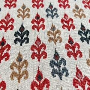 May include: A close-up of a fabric with a repeating pattern of stylized floral motifs in shades of red, brown, black, and white on a cream background.