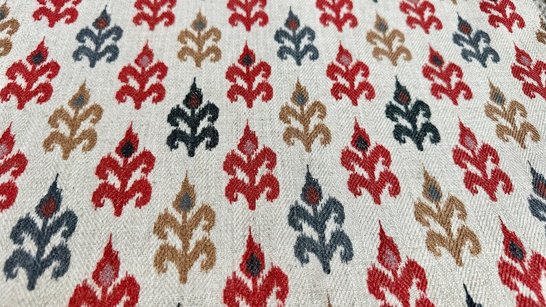 May include: A close-up of a fabric with a repeating pattern of stylized floral motifs in shades of red, brown, black, and white on a cream background.