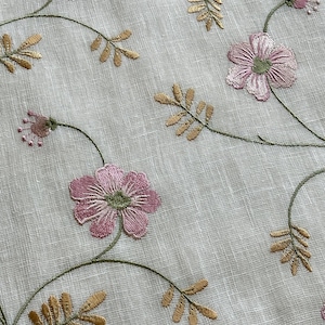 Puede incluir: Tela blanca transparente con flores rosas y hojas doradas bordadas. La tela tiene una textura sutil.