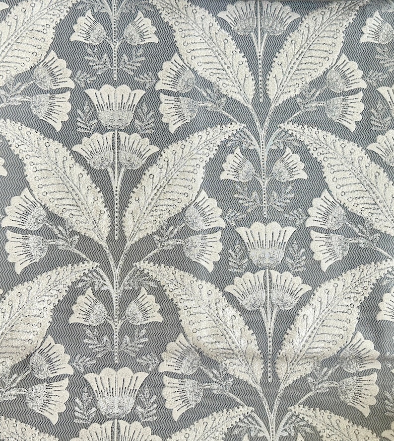 Pu&ograve; includere: Un tessuto grigio con un motivo floreale bianco. Il motivo presenta foglie e fiori stilizzati con un design ripetitivo.