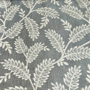 K&ouml;nnte beinhalten: Nahaufnahme eines grauen Stoffes mit einem wei&szlig;en Blumenmuster. Der Stoff hat eine strukturierte Oberfl&auml;che und das Blumenmuster besteht aus kleinen Bl&auml;ttern.