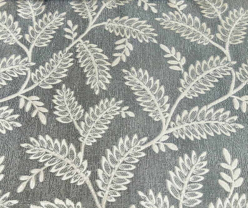 K&ouml;nnte beinhalten: Nahaufnahme eines grauen Stoffes mit einem wei&szlig;en Blumenmuster. Der Stoff hat eine strukturierte Oberfl&auml;che und das Blumenmuster besteht aus kleinen Bl&auml;ttern.