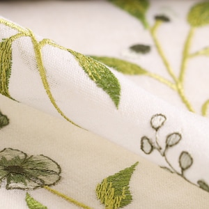 May include: White fabric with green embroidered floral pattern. The fabric is sheer and has a delicate, feminine feel.