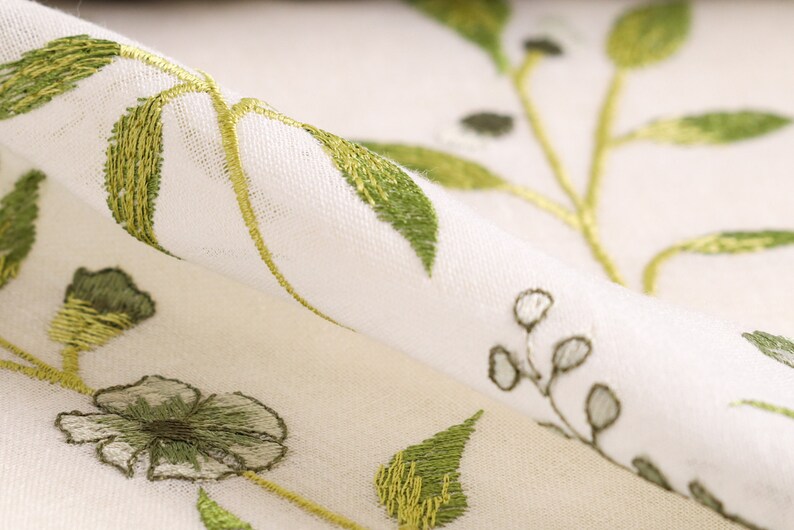 May include: White fabric with green embroidered floral pattern. The fabric is sheer and has a delicate, feminine feel.