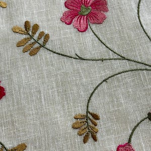 May include: White fabric with embroidered floral design. The flowers are pink and green with brown stems and leaves.