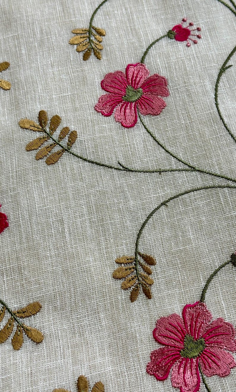 May include: White fabric with embroidered floral design. The flowers are pink and green with brown stems and leaves.
