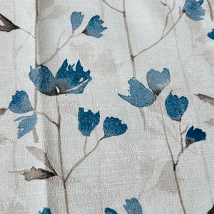 Pu&ograve; includere: Un tessuto bianco con un motivo floreale blu. I fiori sono stilizzati e hanno un effetto acquerello. Lo sfondo &egrave; beige chiaro.