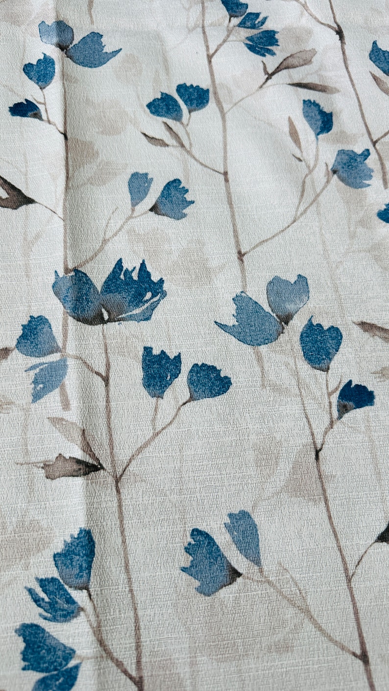 Pu&ograve; includere: Un tessuto bianco con un motivo floreale blu. I fiori sono stilizzati e hanno un effetto acquerello. Lo sfondo &egrave; beige chiaro.