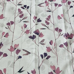May include: A white fabric with a repeating pattern of purple and pink floral sprigs. The fabric has a subtle linen texture.