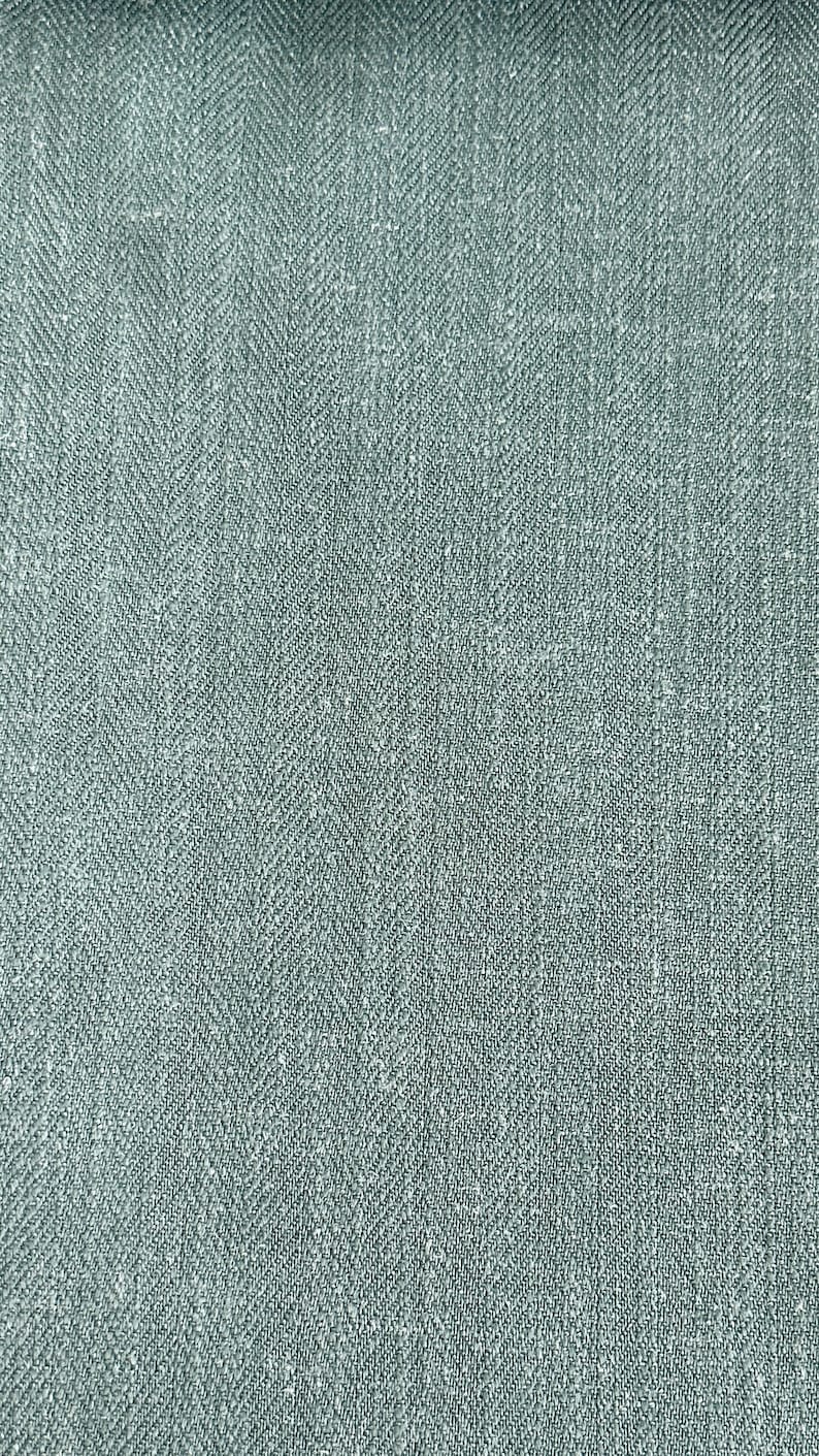 May include: A close-up of a gray herringbone fabric with a subtle sheen. The fabric has a textured, woven appearance.