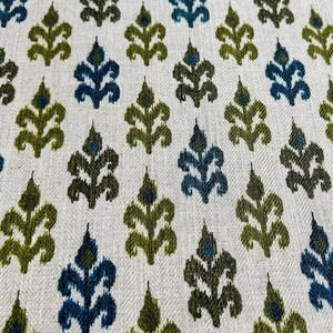 May include: A white fabric with a repeating pattern of green and blue stylized leaves. The fabric has a subtle herringbone weave.
