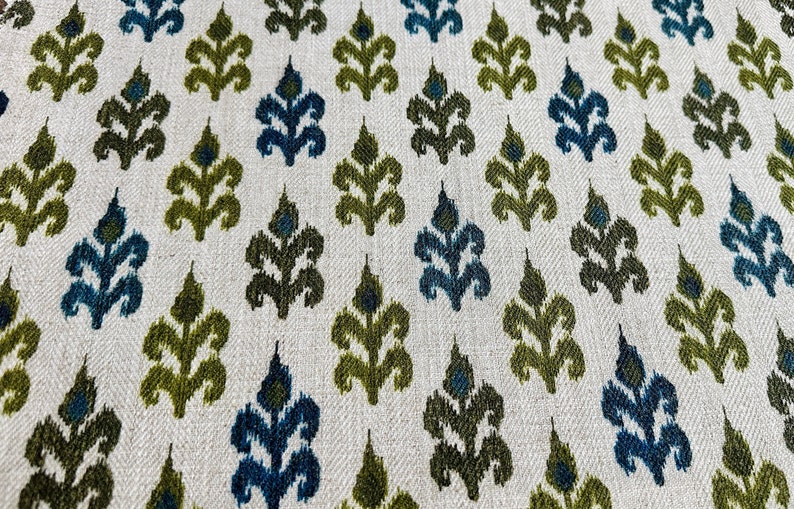May include: A white fabric with a repeating pattern of green and blue stylized leaves. The fabric has a subtle herringbone weave.