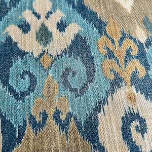 May include: Close-up of a fabric with a blue, brown, and white ikat pattern. The fabric has a woven texture and a subtle herringbone pattern.