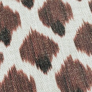 May include: Close-up of a white fabric with a brown animal print pattern. The print resembles a leopard or cheetah pattern.