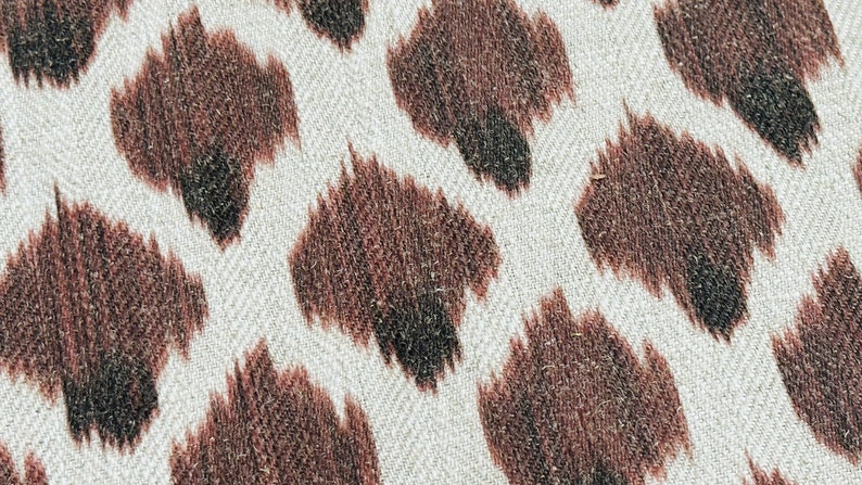 May include: Close-up of a white fabric with a brown animal print pattern. The print resembles a leopard or cheetah pattern.