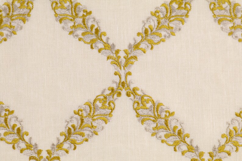 May include: A white fabric with a repeating pattern of gold and silver embroidered floral designs. The design is a series of connected swirls and leaves.