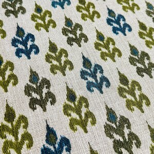 May include: A close-up of a fabric with a repeating pattern of green and blue stylized floral motifs on a white background.