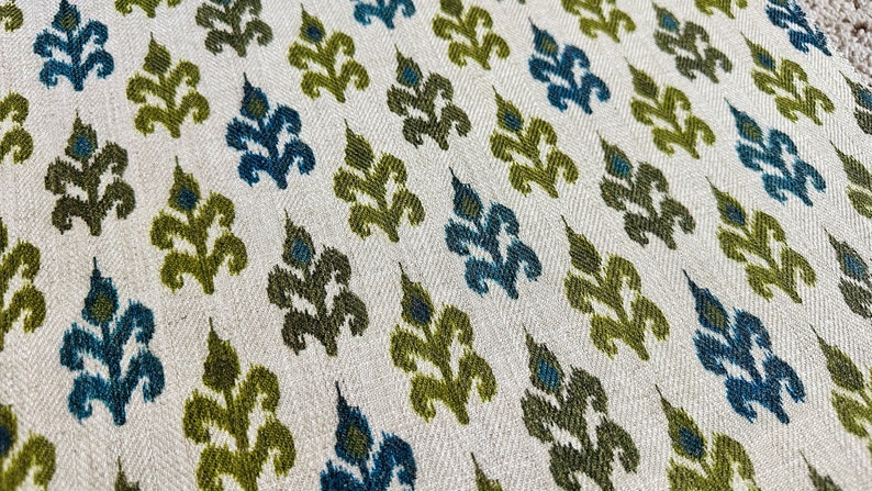 May include: A close-up of a fabric with a repeating pattern of green and blue stylized floral motifs on a white background.
