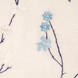 May include: White fabric with embroidered blue and white flowers. The flowers are arranged on dark blue stems.