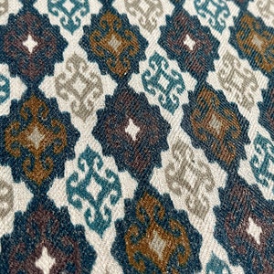 May include: A close-up of a fabric with a repeating pattern of brown, blue, and white geometric shapes. The fabric has a textured surface.