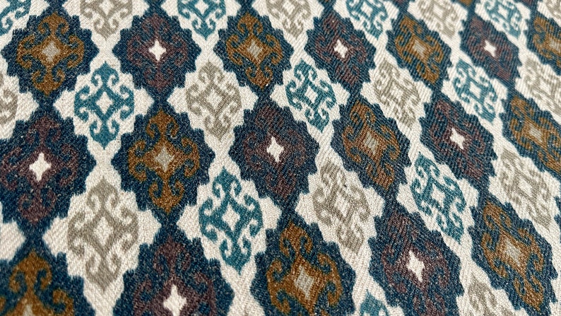 May include: A close-up of a fabric with a repeating pattern of brown, blue, and white geometric shapes. The fabric has a textured surface.