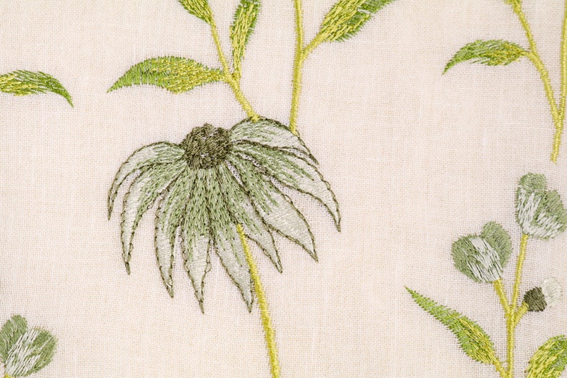 May include: A close-up of a white fabric with green embroidered flowers. The flowers have a delicate, layered design and are accented with a light green color.