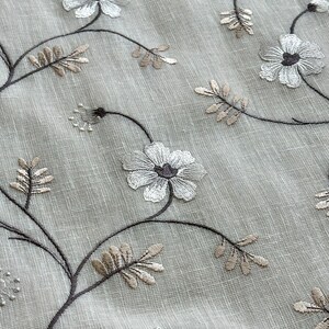 May include: A close-up of a sheer white curtain with embroidered brown and white floral designs.