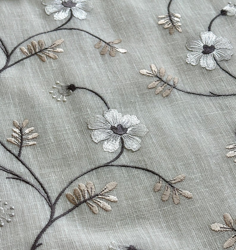 May include: A close-up of a sheer white curtain with embroidered brown and white floral designs.