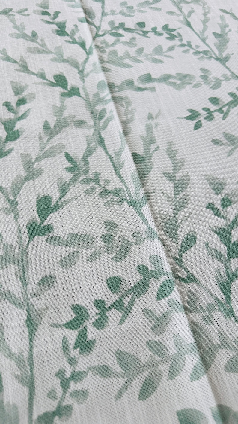 May include: White fabric with a green leafy pattern. The fabric has a subtle texture and the leaves are a light green color.