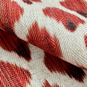 May include: Red and black ikat patterned fabric with a white background. The fabric has a herringbone weave.