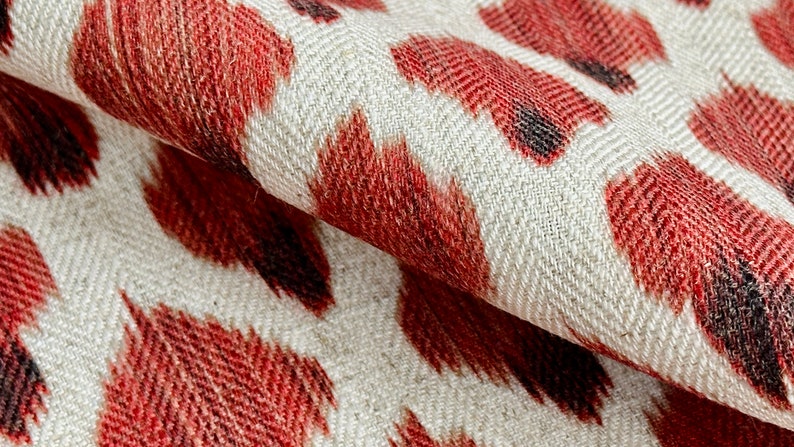 May include: Red and black ikat patterned fabric with a white background. The fabric has a herringbone weave.