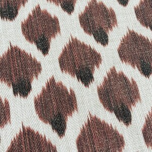 May include: Close-up of a white fabric with a brown and black animal print pattern. The pattern resembles a leopard print.